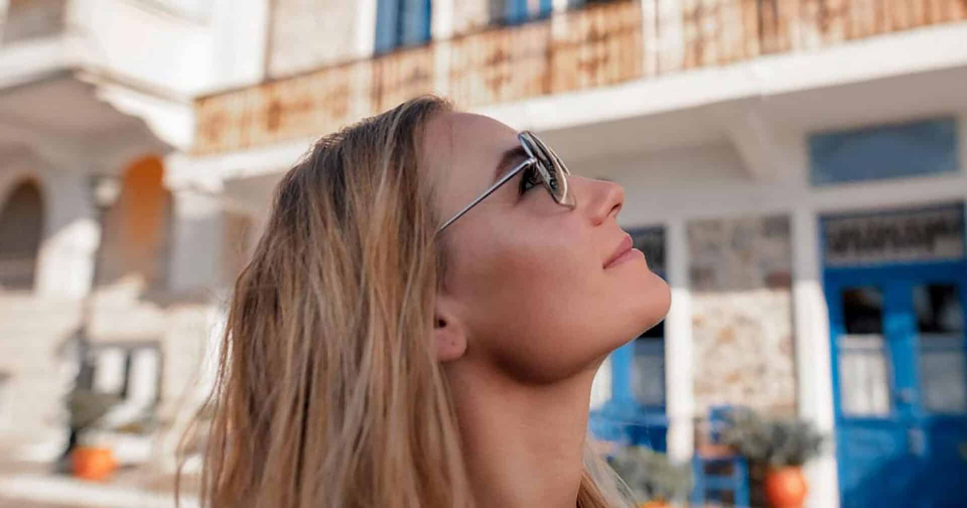 A girl in sunglasses looking up to the sky in front of a blue and white building