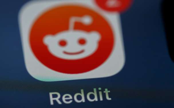 Close-up of the Reddit app icon on a screen, showing the Reddit logo with a notification badge displaying the number 2 in the top right corner. The word Reddit appears below the icon.