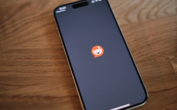 A smartphone on a wooden table displays the Reddit app loading screen, showing the Reddit logo on a dark background.