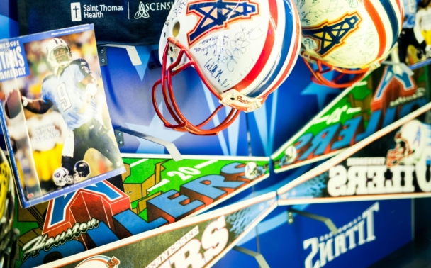 Display case with Houston Oilers and Tennessee Titans football helmets, pennants, and a photograph of a player in uniform. The background features blue team branding and logos.