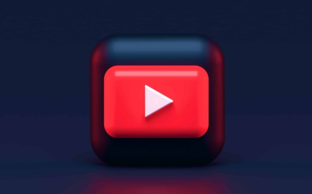 A 3D red and black cube with a white play button symbol centered on its front face, resembling a stylized YouTube logo, set against a dark blue background.