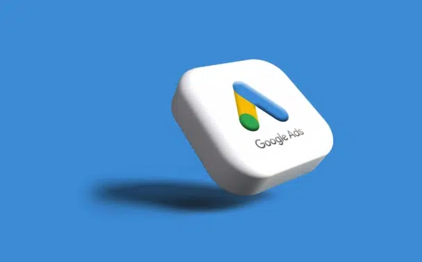 A 3D white square with the Google Ads logo and Google Ads text on it, floating over a blue background with a shadow beneath.